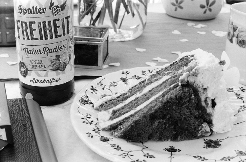 A slice of cake and a bottle of Spalter Freiheit radler on a laid table, shot on black and white 35mm film