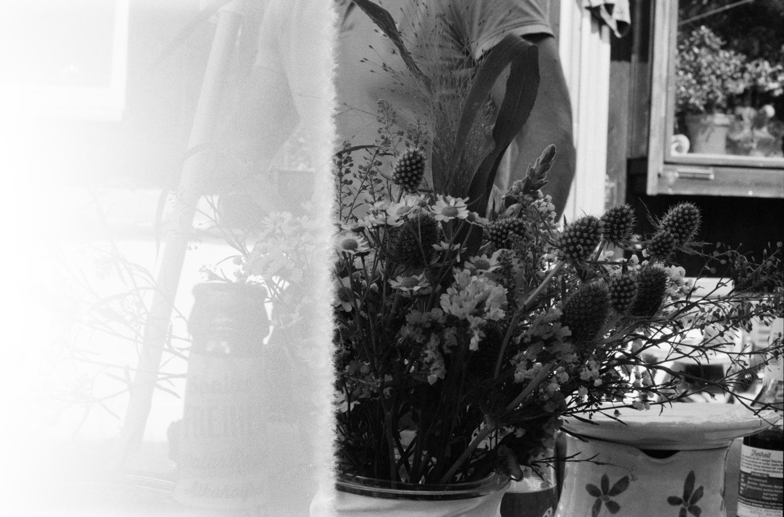 A bunch of wild flowers in a jar by a window, with a light leak across the left of the frame, shot on black and white 35mm film